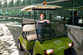 Security guard sitting in golf cart in front of glass building.